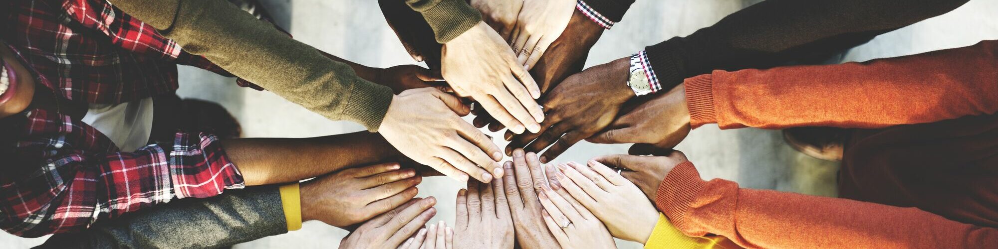 Eine Gruppe verschiedener Menschen legt die Hände übereinander.