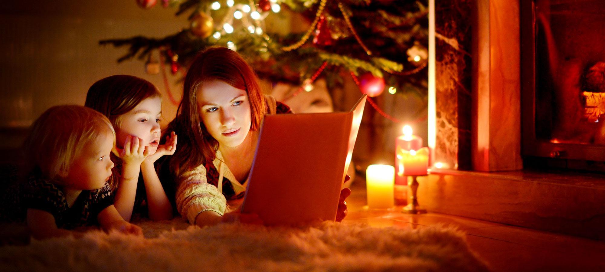 Eine Mutter liest ihren Kindern an Weihnachten die Weihnachsgeschichte unterm Tannenbaum vor