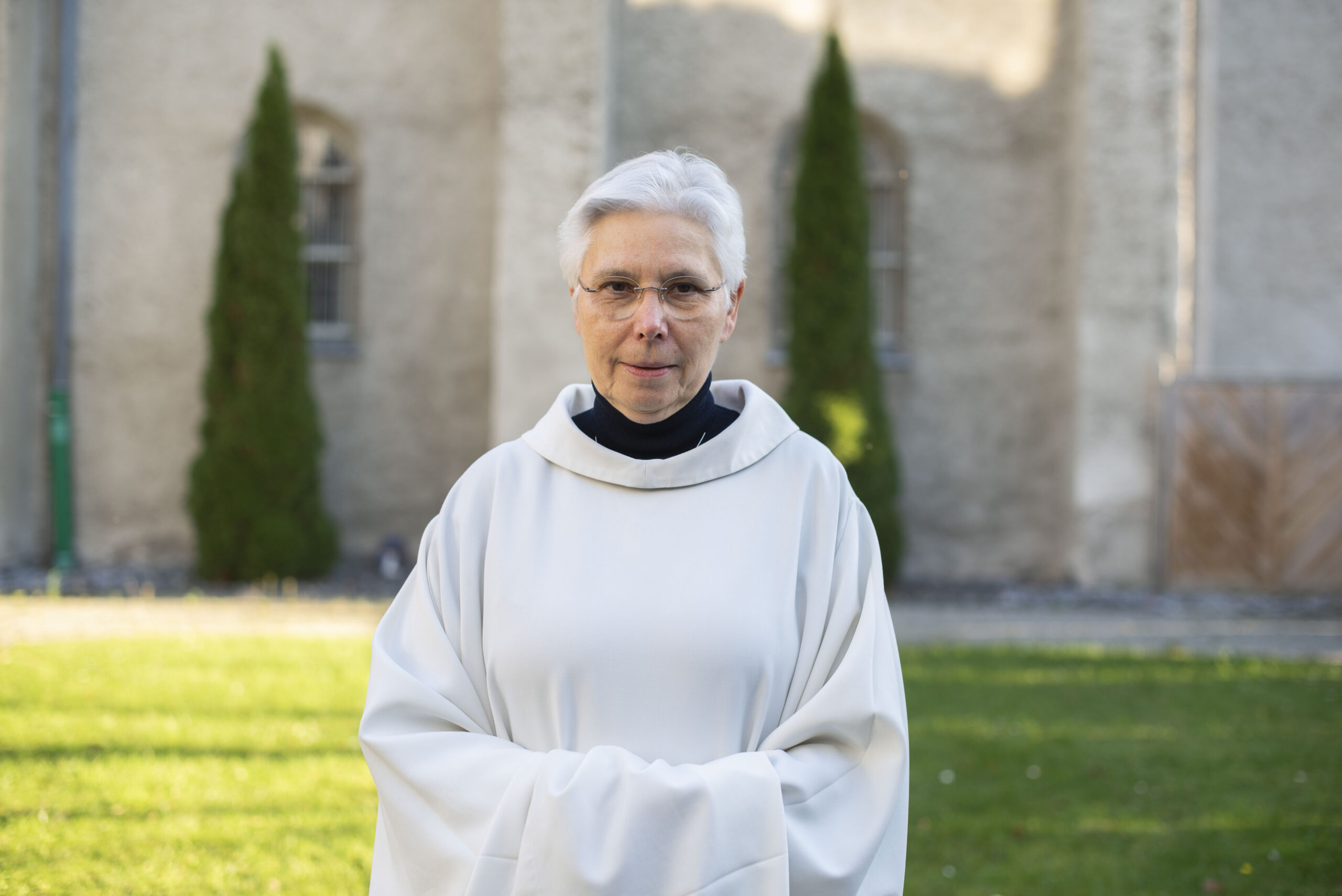 Die Augustiner Chorfrau Sr. M. Ancilla Ernstberger steht in einem weißen Gewand im Garten des Michaelsklosters Paderborn