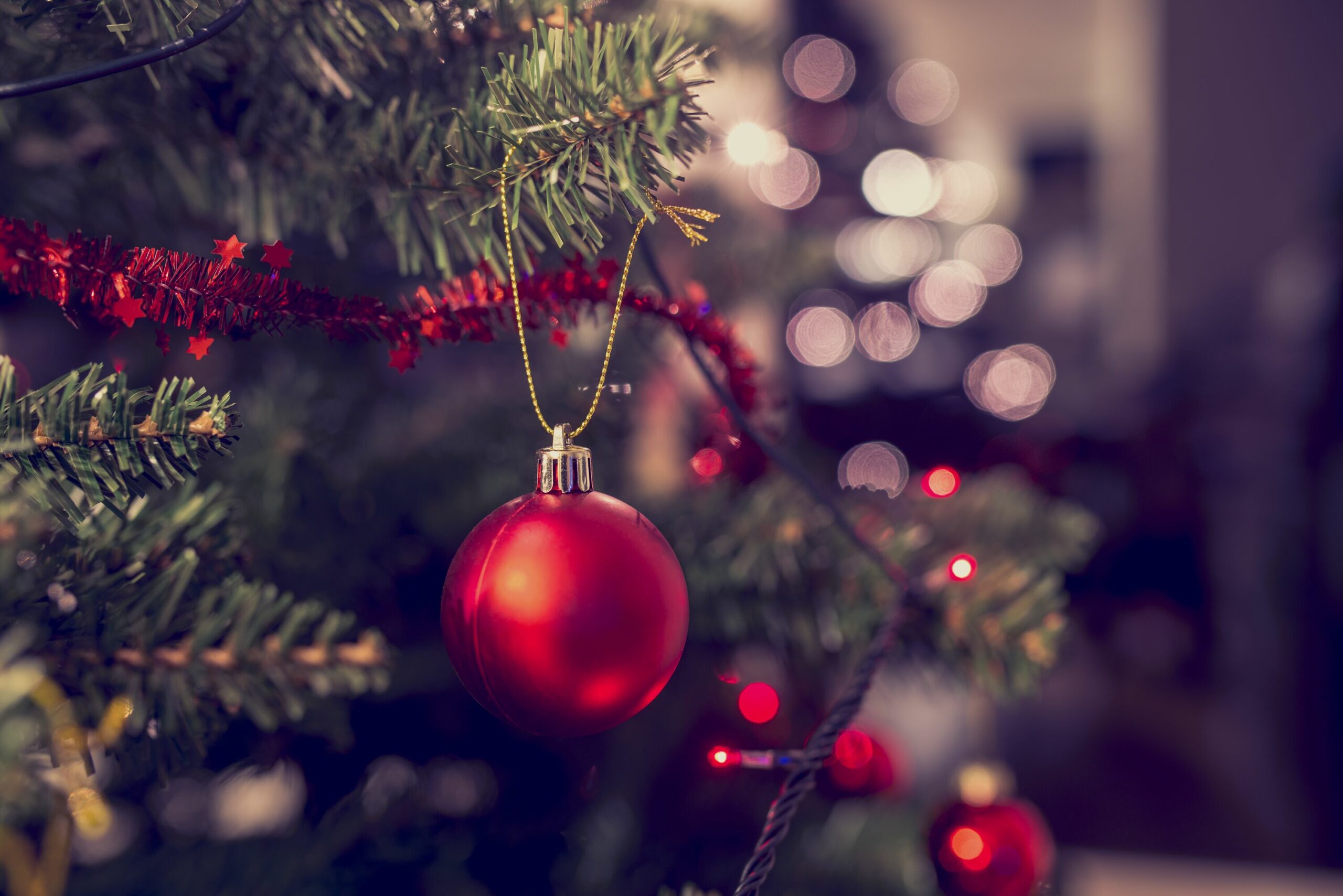 Detail einer roten Christbaumkugel, die an einem verzierten Weihnachtsbaum hängt.