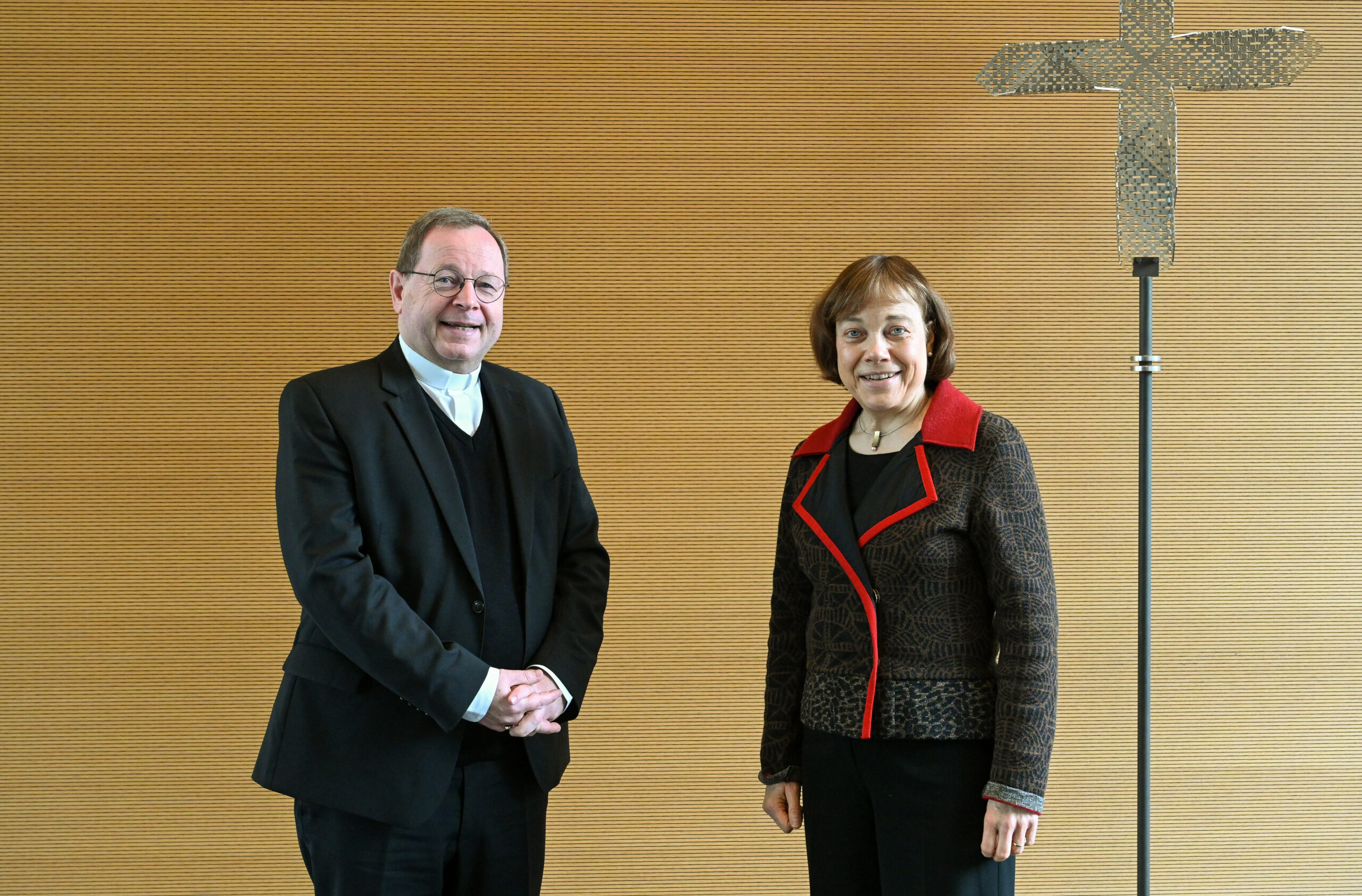 Bischof Bätzing und Präses Kurschus vor Holzwand mit Kreuz