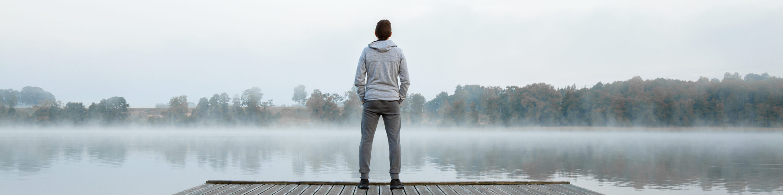 Mann steht auf einem Steg an einem nebeligen See