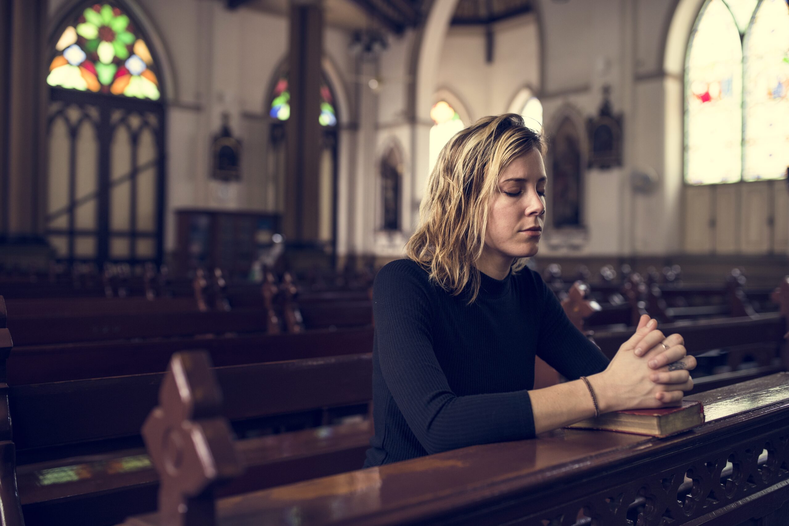 Eine junge Frau betet kniend in einer leeren Kirche