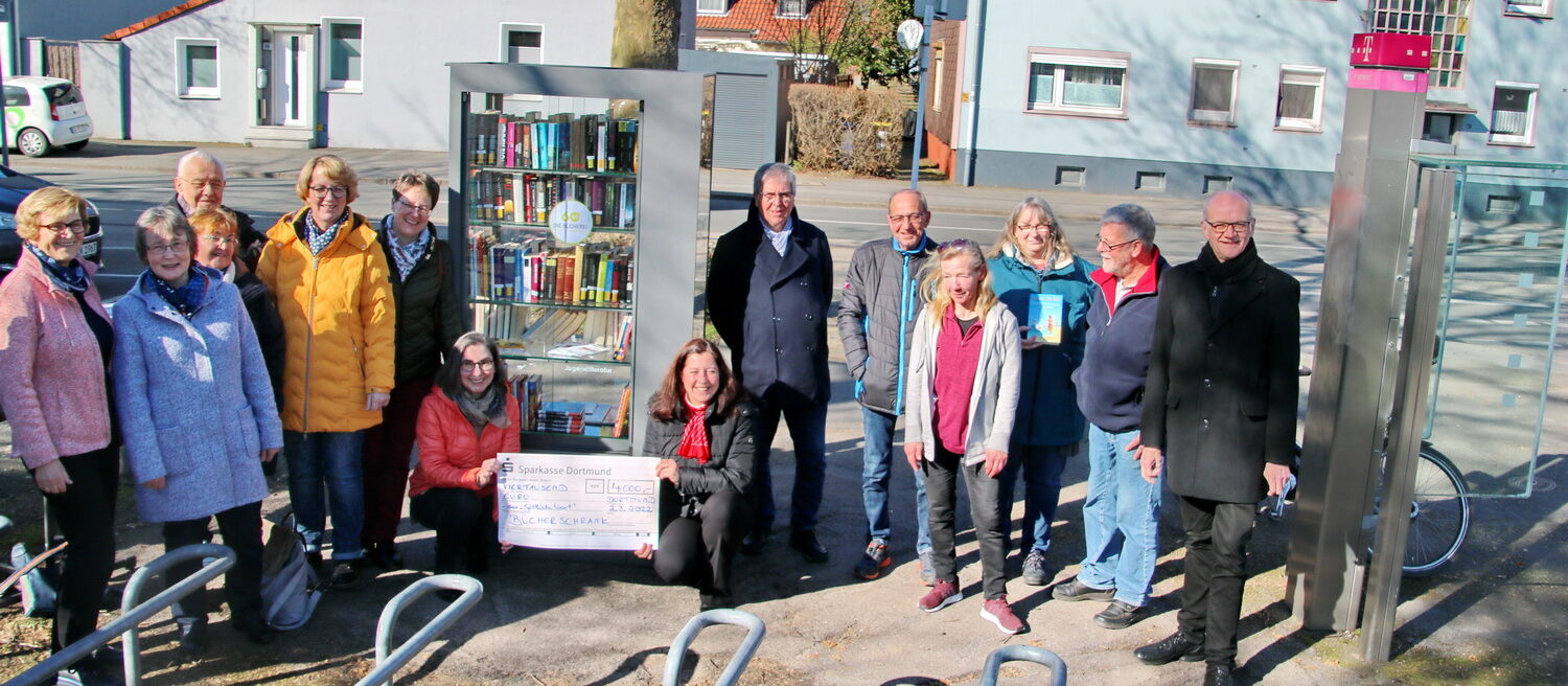 Menschen in einem Halbkreis, in der Mitte ein Bücherschrank