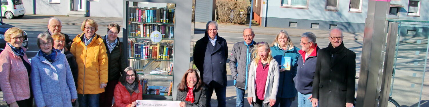 Menschen in einem Halbkreis, in der Mitte ein Bücherschrank