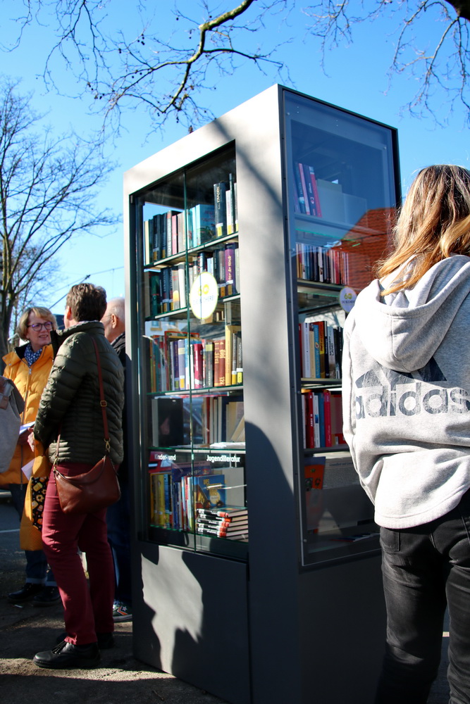 Bücherschrank umgeben von Menschen in der Natur