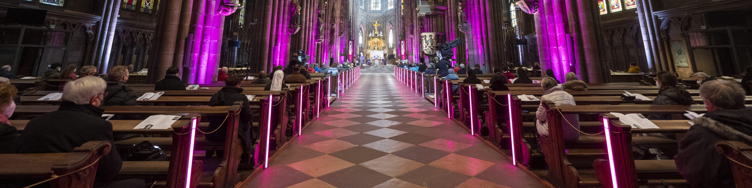 Viele Menschen in einer Kirche, lila Beleuchtung, Goldenes Kreuz im Hintergrund