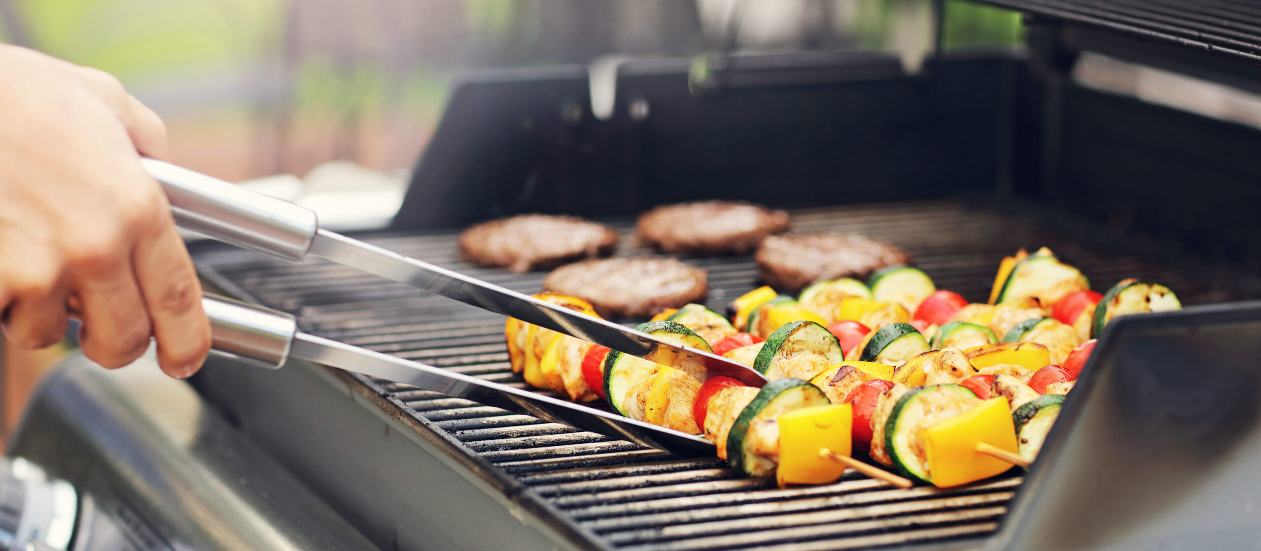 Blick auf einen Grill mit Fleisch und Gemüsespießen.