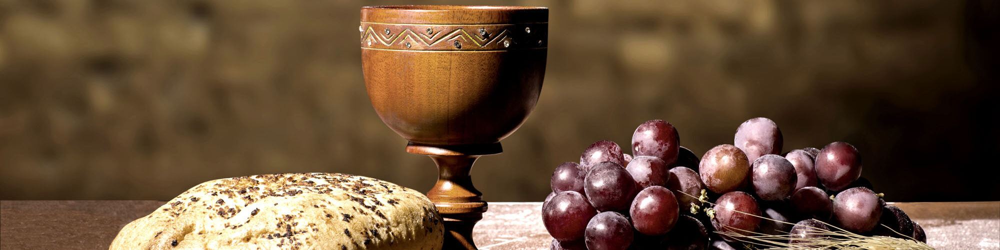 Auf einem Tisch befinden sich ein Laib Brot, ein Kelch und Weintrauben