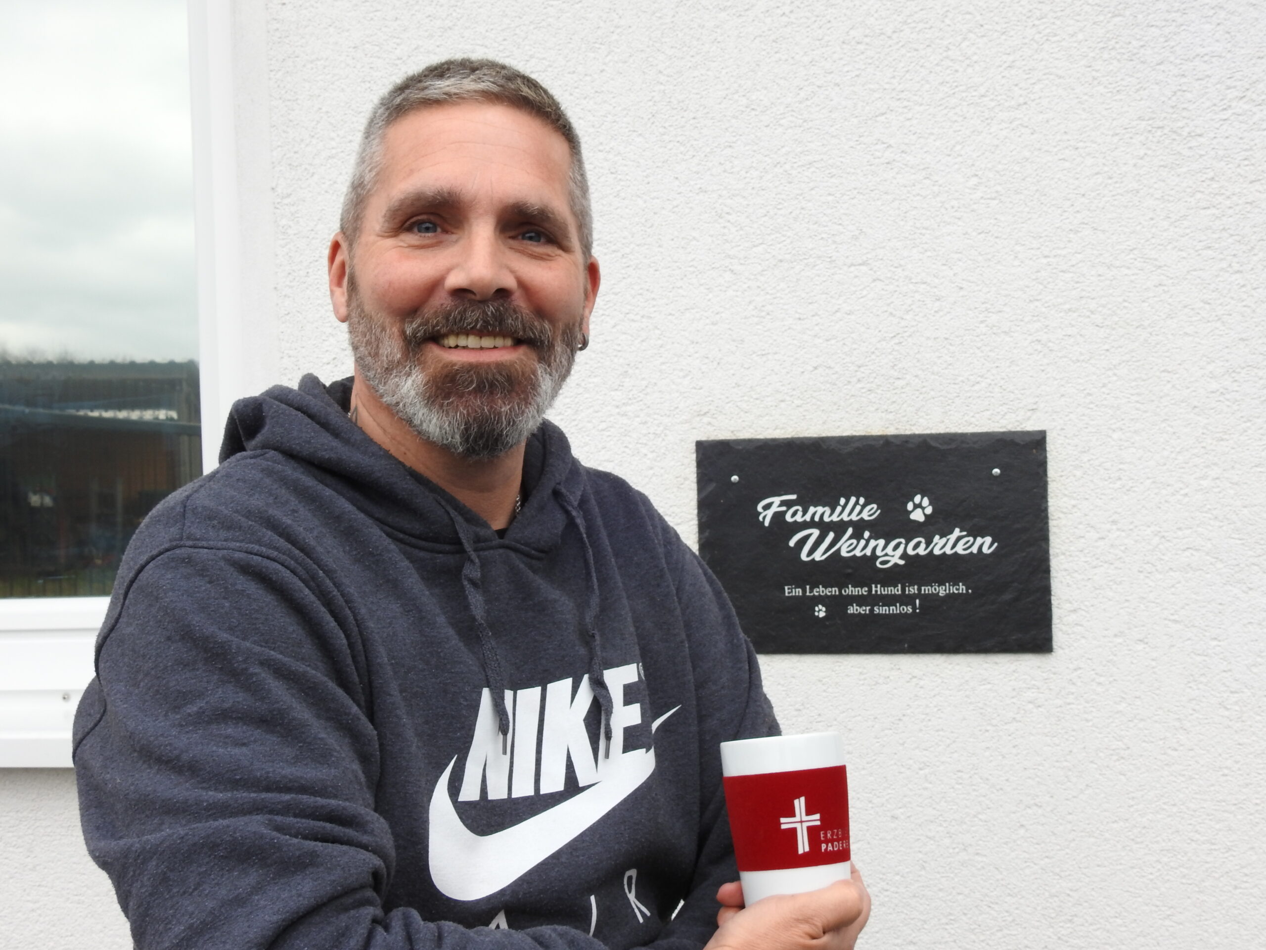Christoph Weingarten vor seinem Haus. In der Hand hält er einen Kaffeebecher vom Erzbistum Paderborn.