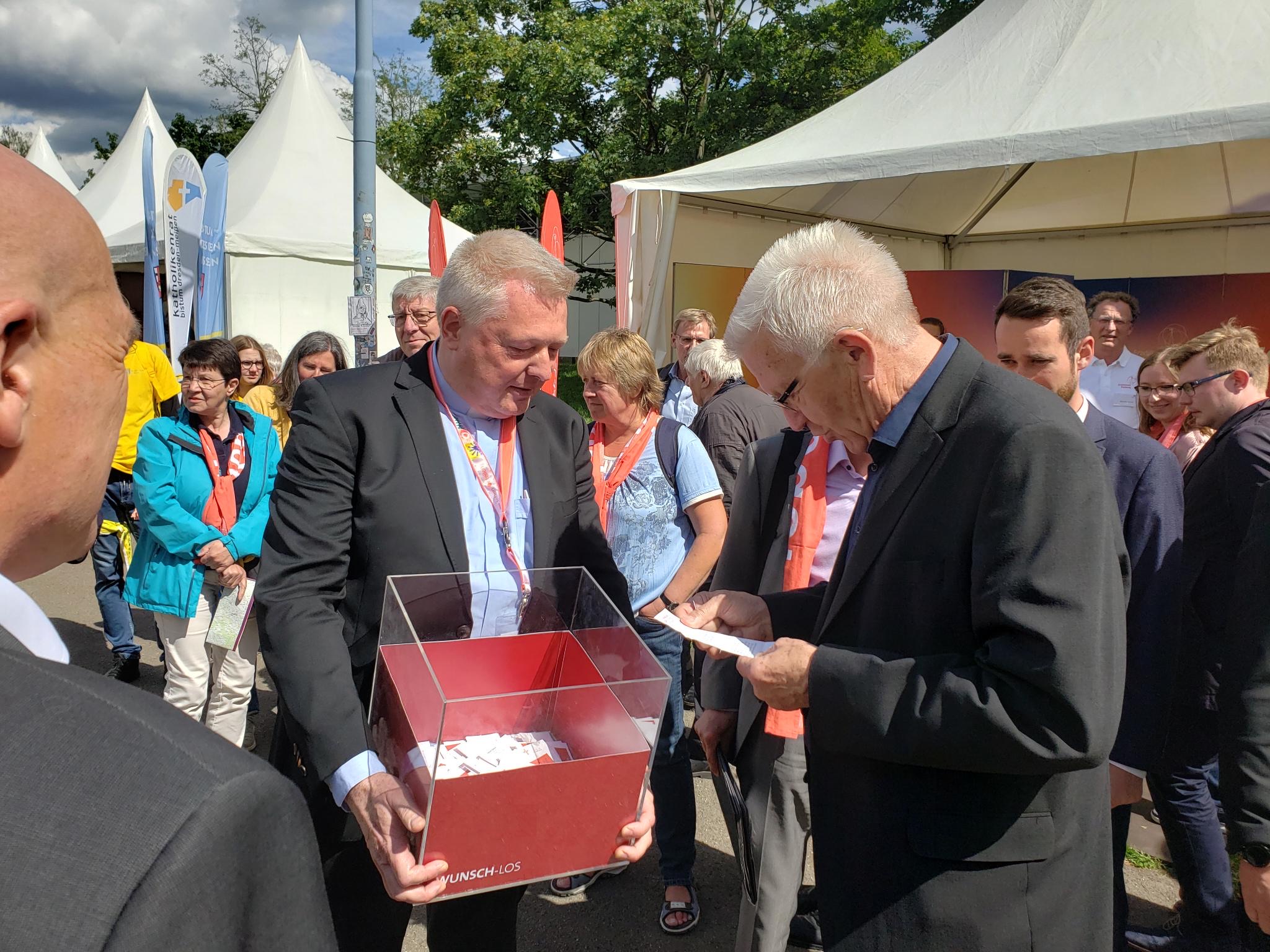 Auch Baden-Württembergs Ministerpräsident Winfried Kretschmann besuchte den Stand von Paderborn und zog ein Wunschlos aus der Box, die Msgr. Dr. Bredeck ihm reichte.