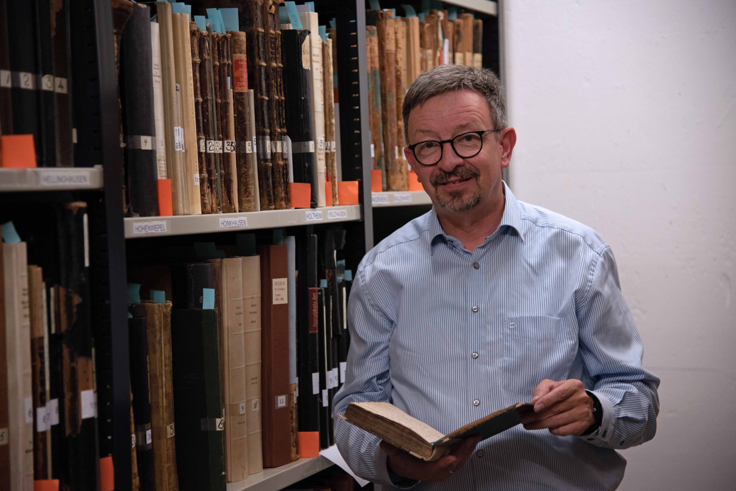 Michael Streit hält ein Buch in der Hand und steht vor einem Regal mit augenscheinlich alten Büchern