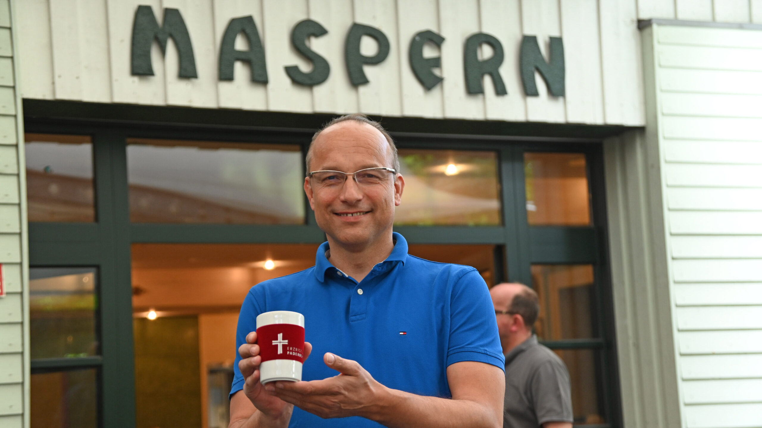 Hubert Salmen steht vor einem Gebäude und hält einen Kaffeebecher in der Hand.