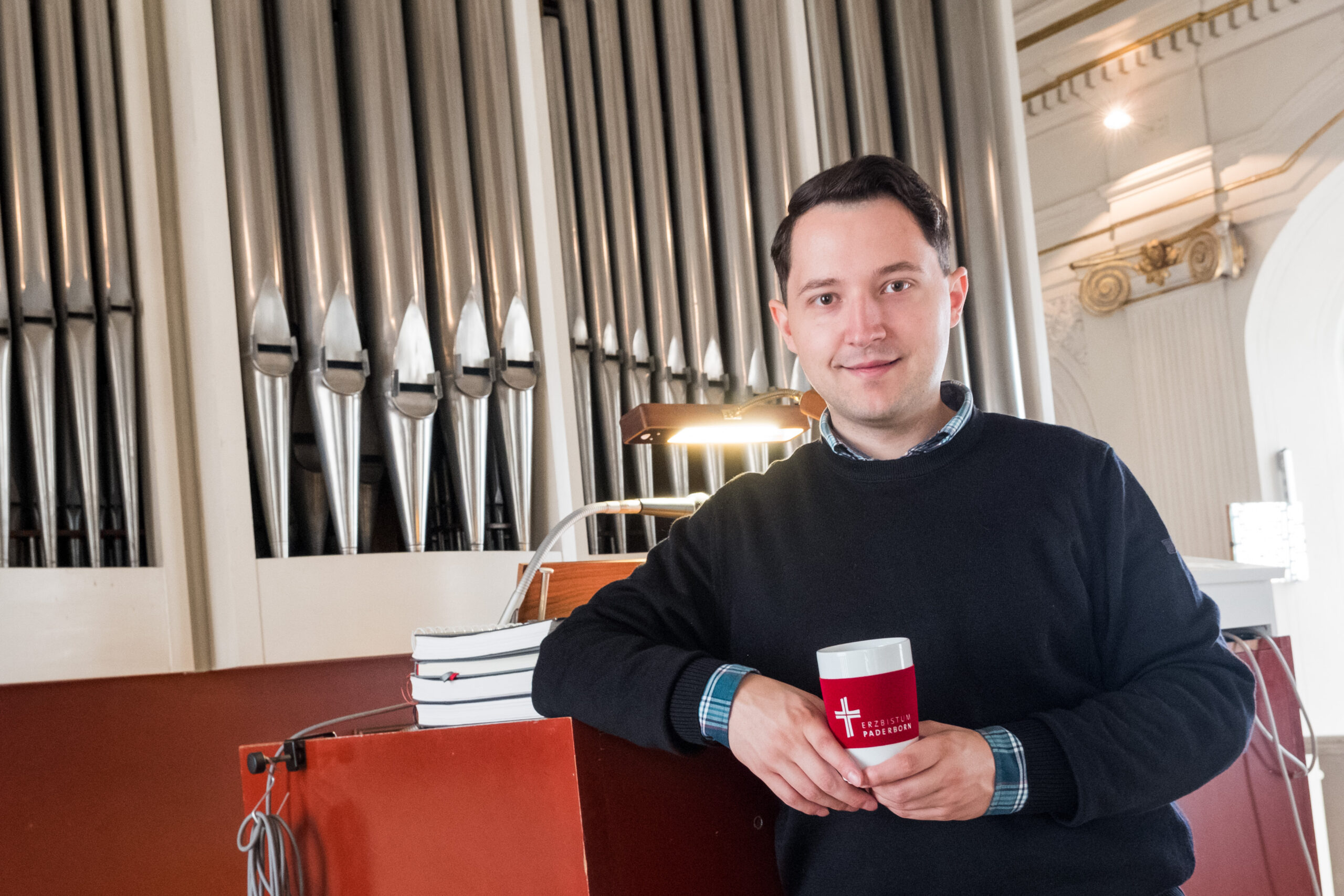Ivo Kanz steht vor einer Orgel. Im Hintergrund sieht man die Orgelpfeifen.