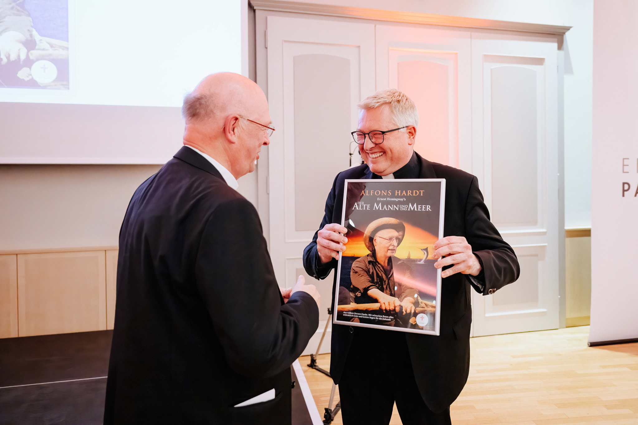 Diözesanadministrator Msgr. Dr. Michael Bredeck überreicht ein Filmplakat von "Der Alte Mann und das Meer" als Geschenk.