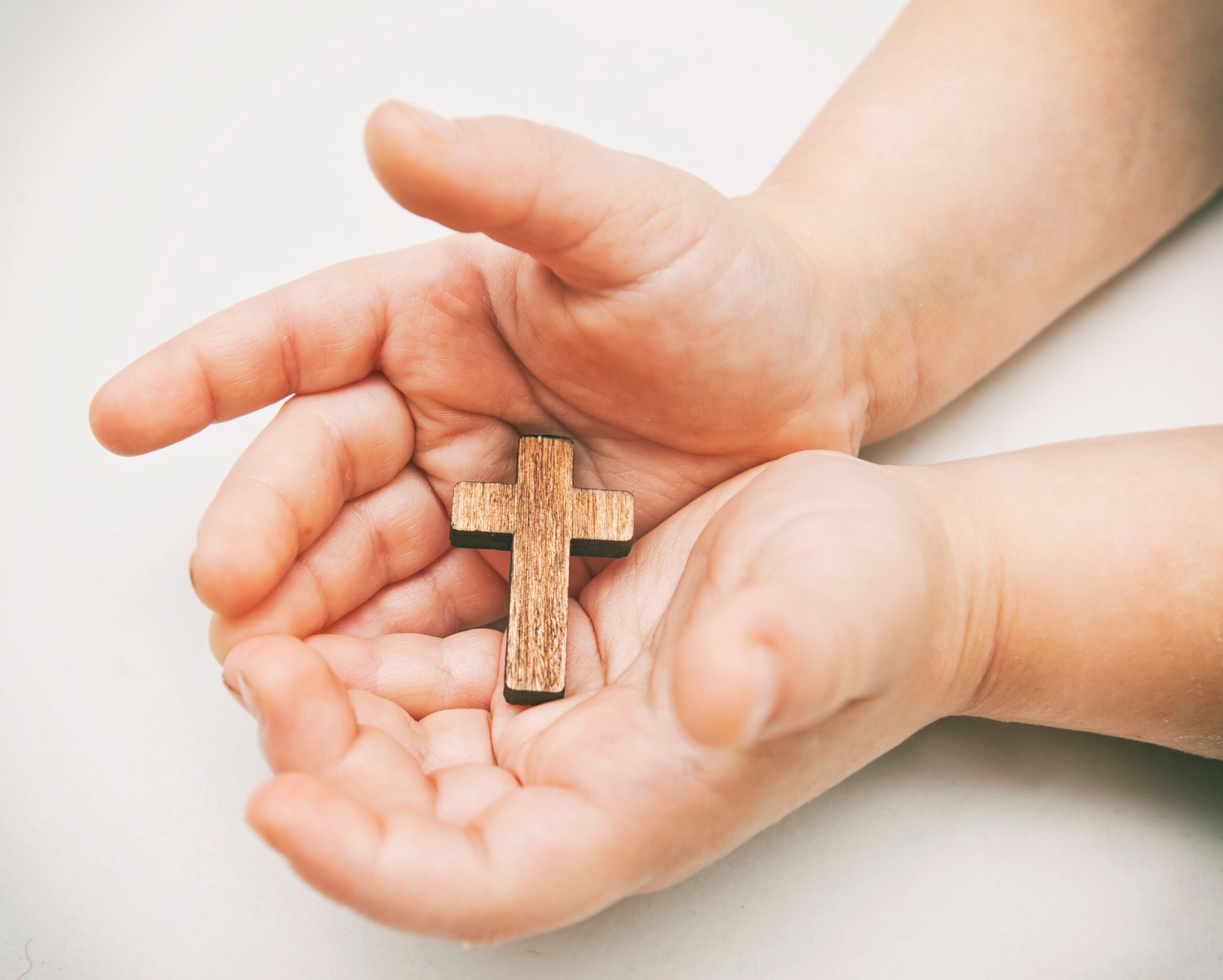 Ein kleines Holzkreuz in den Händen des Kindes
