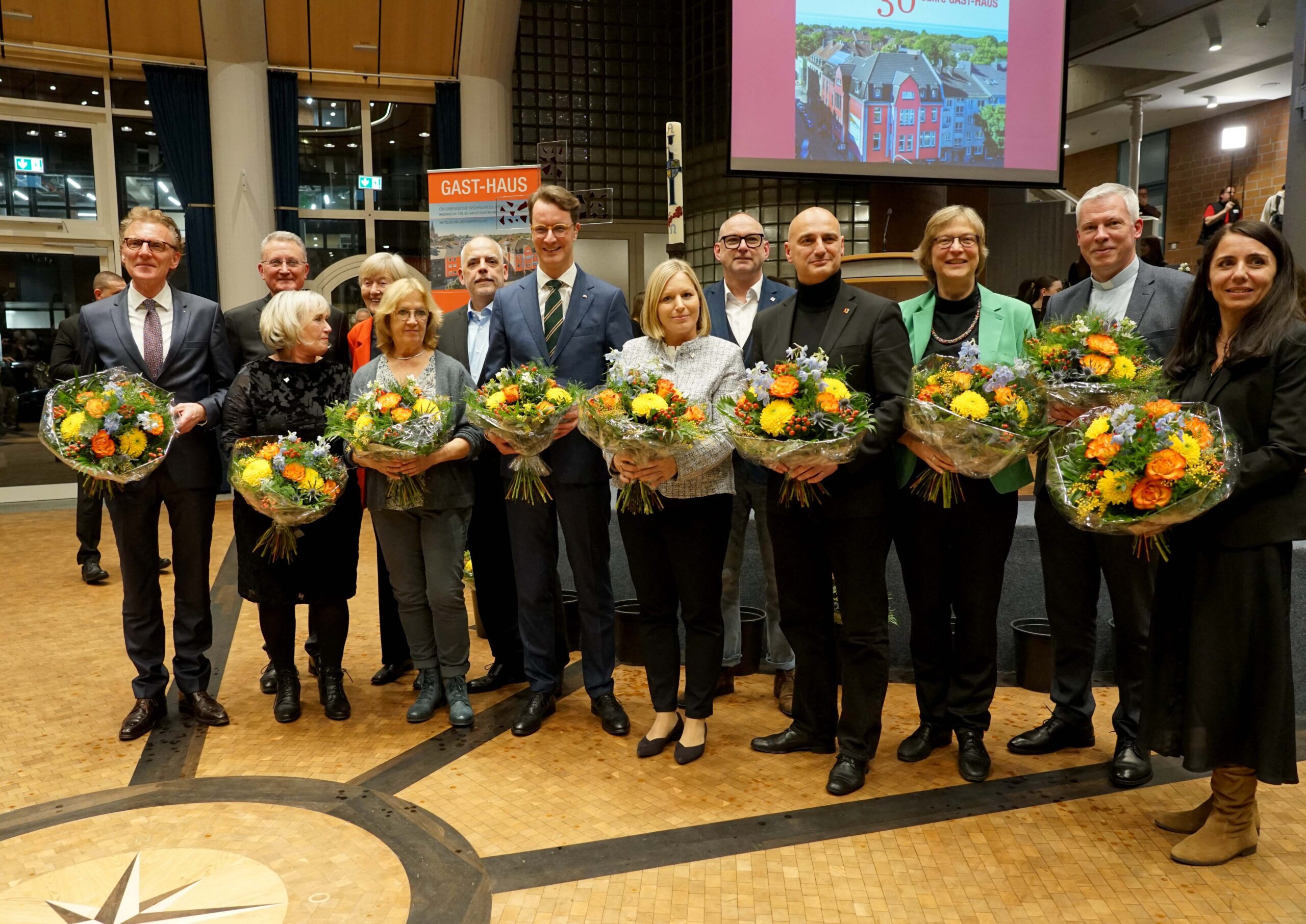 Festakt „30 Jahre Gast-Haus statt Bank“ im Dortmunder Mallinckrodt-Gymnasium mit NRW-Ministerpräsident Hendrik Wüst (vorne, 4. v.l.), Dompropst Monsignore Joachim Göbel (hinten, 1.v.l.), Schulleiter Christoph Weishaupt (vorne, 1. v.l.) und Gast-Haus-Geschäftsführerin Katrin Lauterborn (vorne, 5. v.l.) sowie weiteren Beteiligten. Foto: Michael Bodin / Erzbistum Paderborn