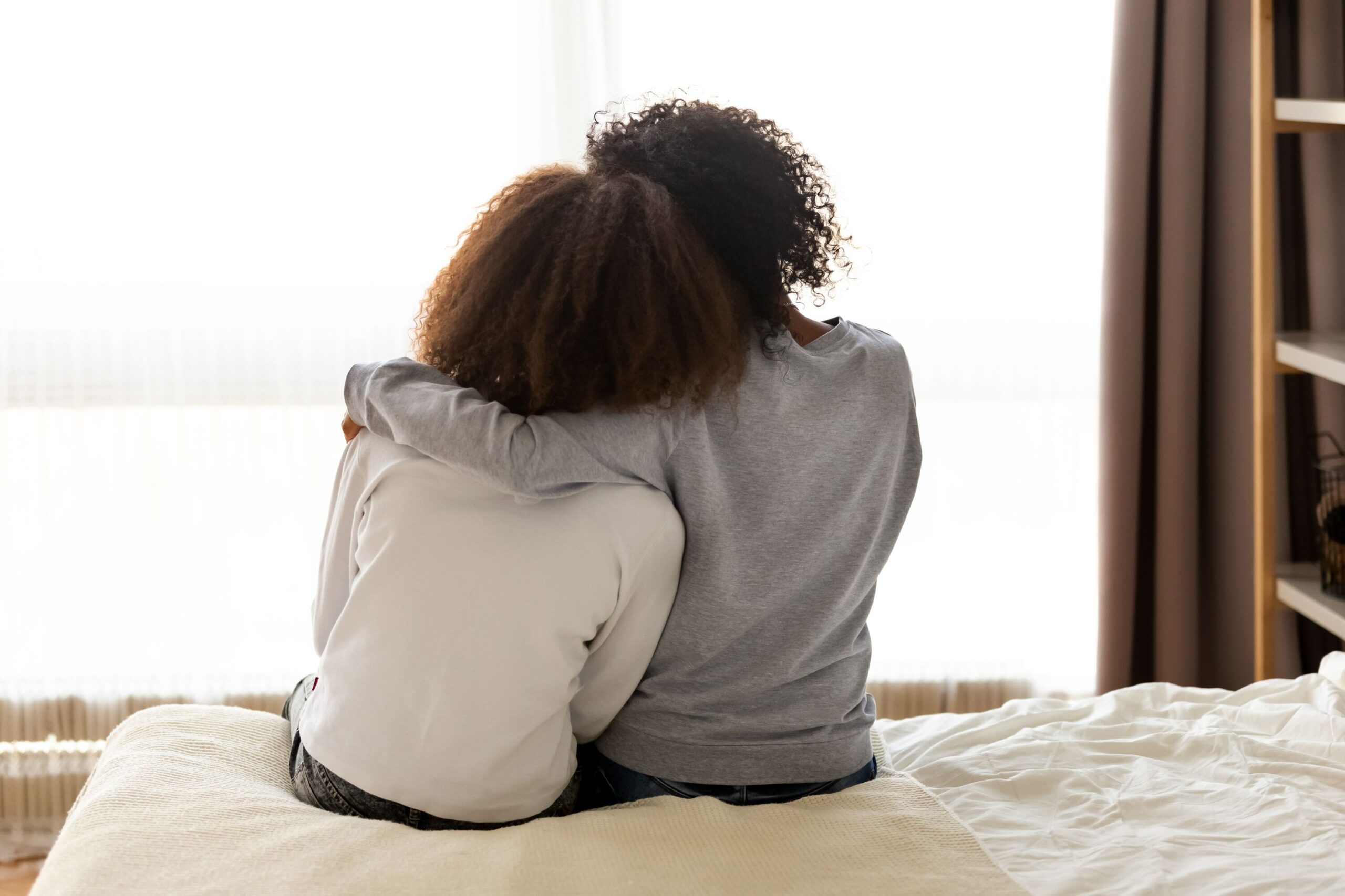 Von hinten zu sehen: Mutter und Tochter umarmen sich auf dem Bett zu Hause