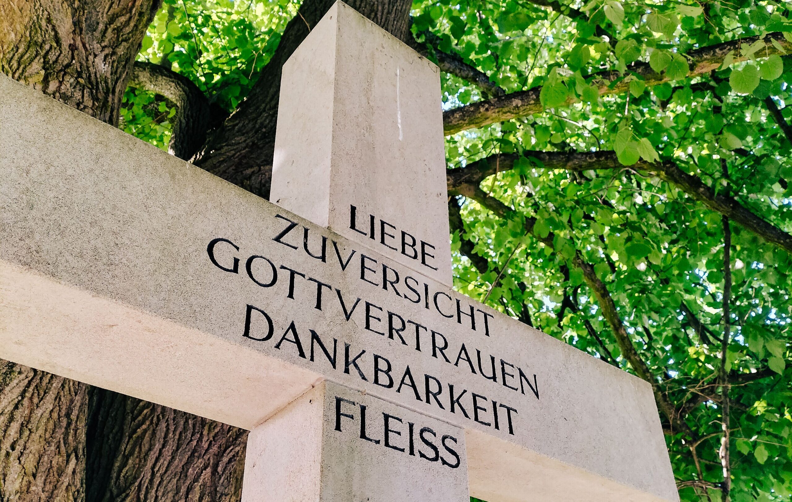Nahaufnahme eines Kreuzes. Fünf Wörter sind dort eingeprägt: Liebe, Dankbarkeit, Zuversicht, Gottvertrauen und Fleiß