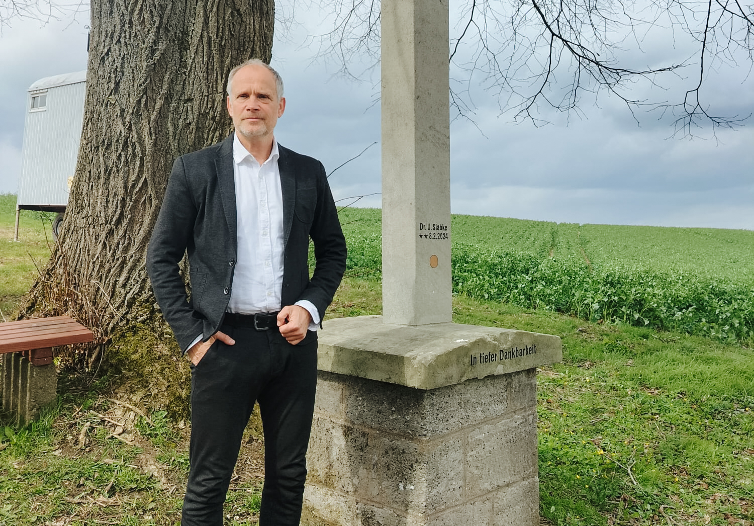 Porträtaufnahme eines Mannes in Anzug, der vor einem Kreuz steht