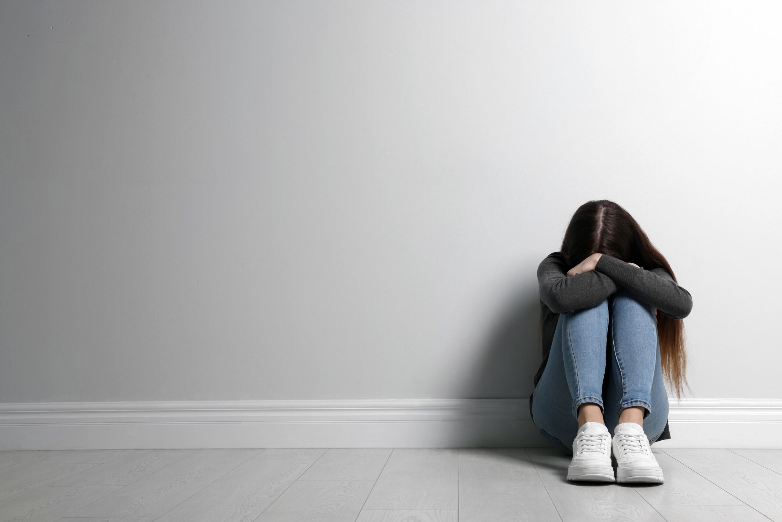 Teenager-Mädchen sitzt auf dem Boden neben der Wand und versteckt sein Gesicht. Platz für Text