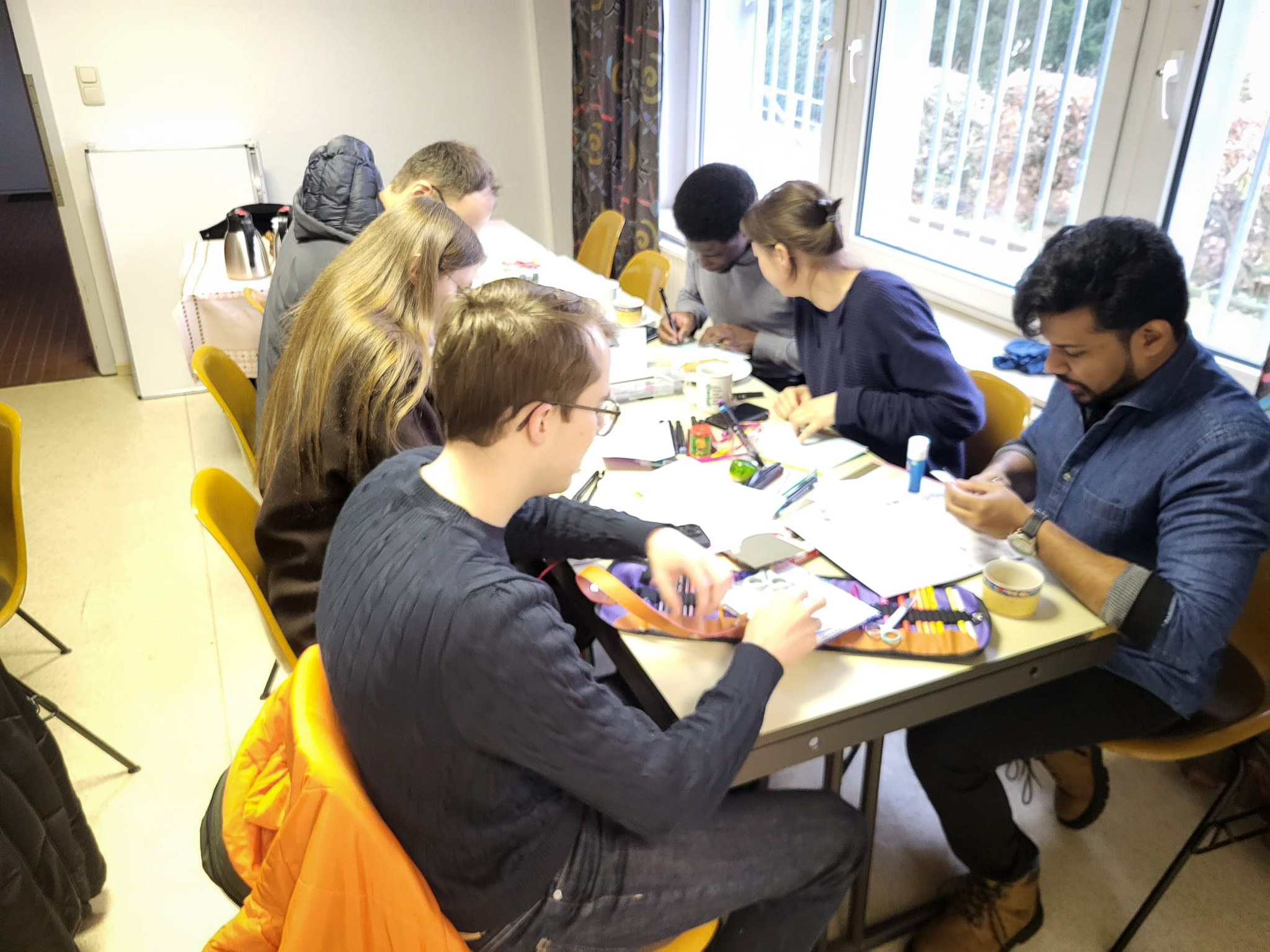 Mitglieder von Come and see sitzen gemeinsam an einem Tisch und gestalten etwas mit Papier und Stiften.