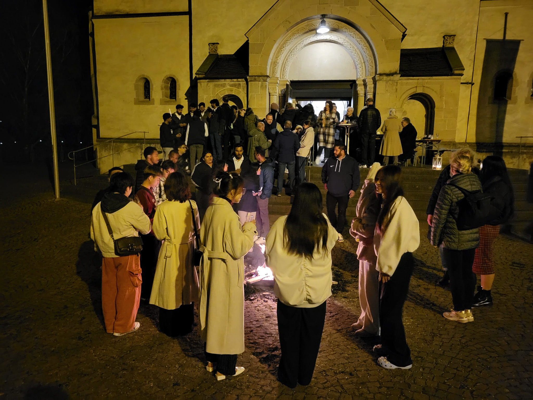 Mitglieder von Come and see stehen abends vor der Kirche und machen ein Feuer.