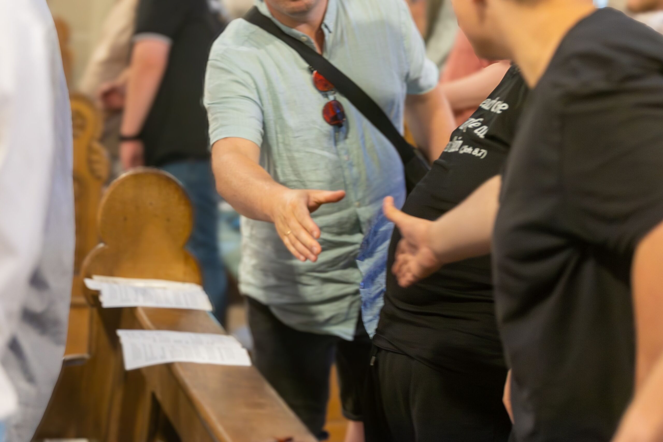 Menschen, die in einer Kirchenbank stehen, reichen sich die Hand.