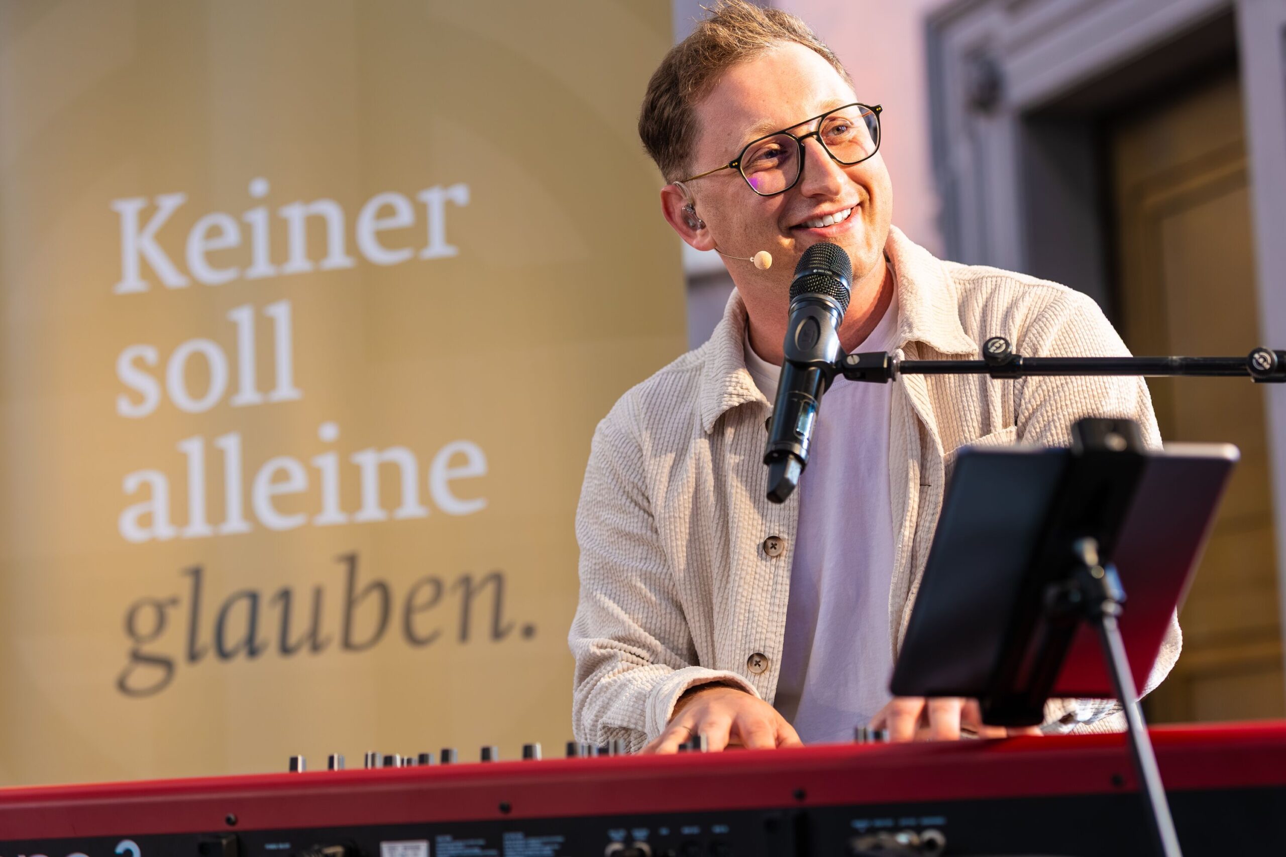 Nahaufnahme eines jungen Sängers mit Brille vor einem Keybord mit Mikrofon