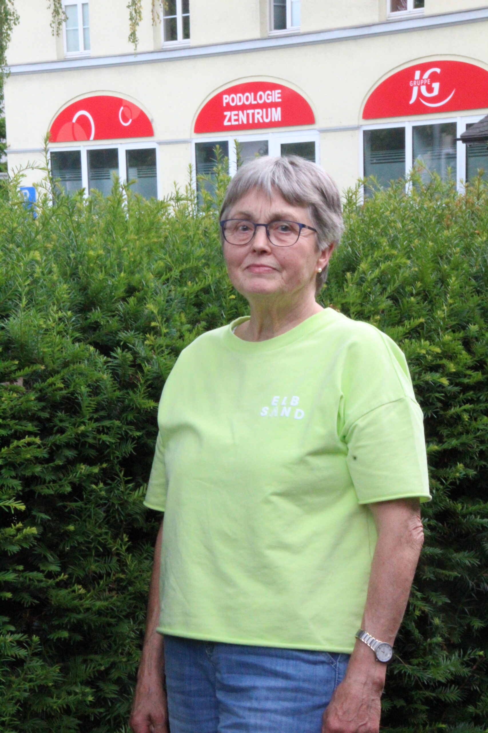 Elisabeth Wächter steht draußen vor einer Hecke