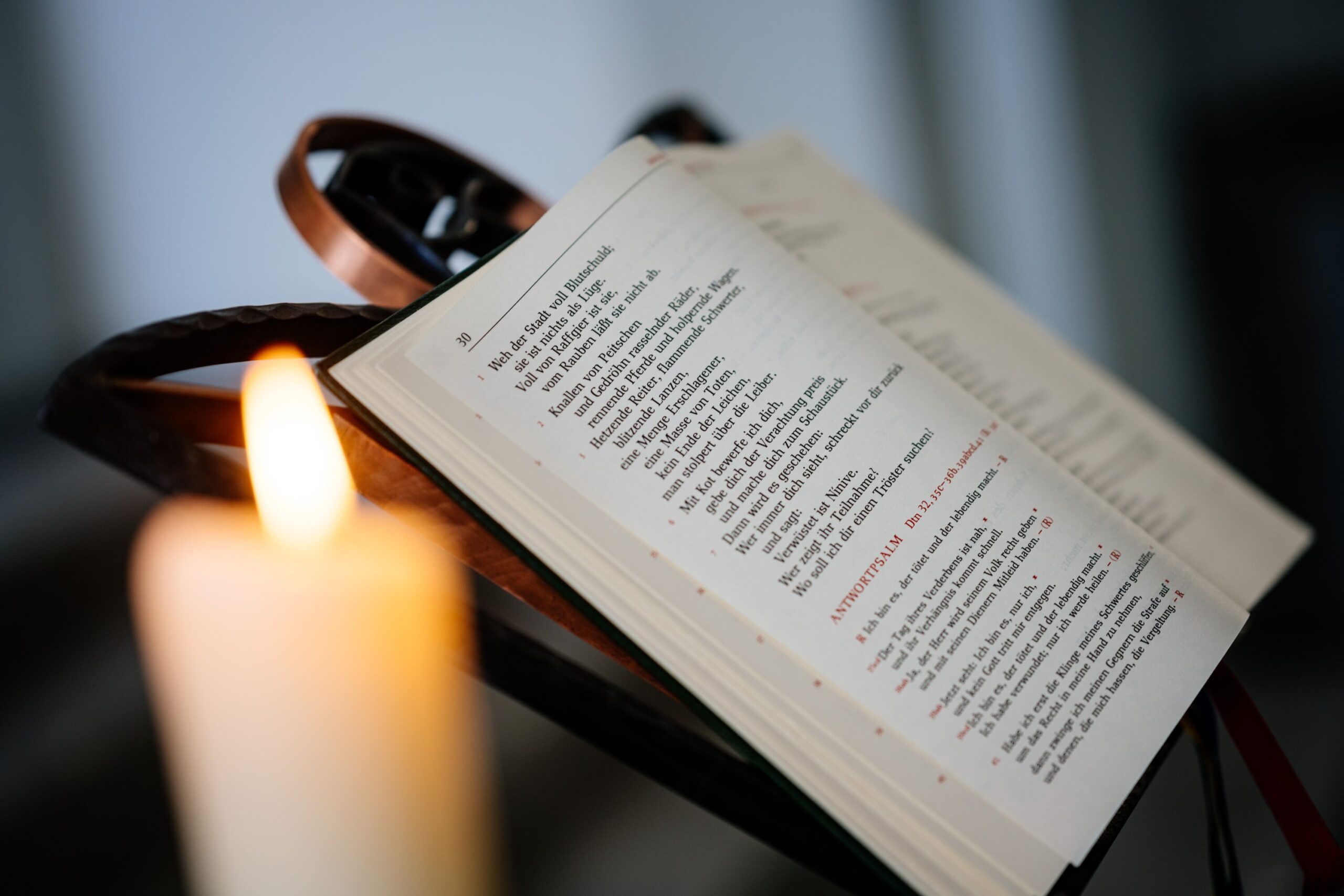 Im Hintergrund sieht man ein aufgeschlagenes Buch, davor einen verschwommene angezündete Kerze