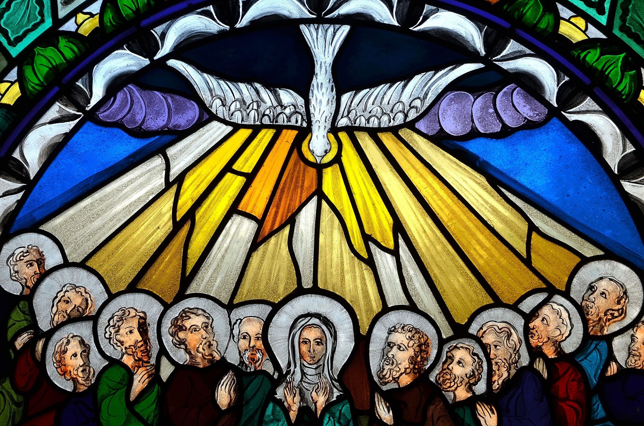 Ein Glasfenster auf dem Die Jünger zu sehen sind. Darüber ein Vogel der goldene Strahlen zu den Köpfen der Jünger schießt