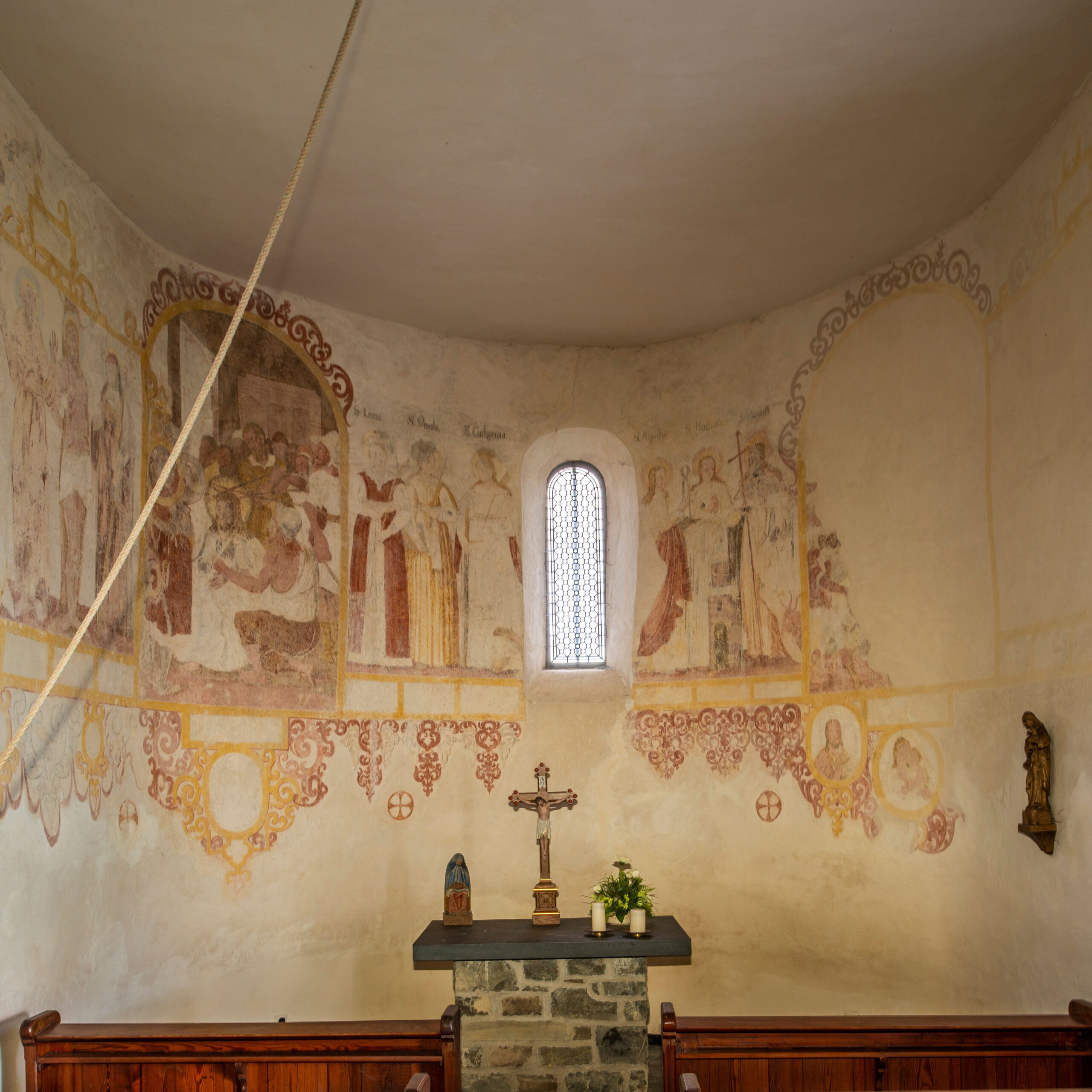 Innenraum einer Kapelle mit historischen Wandmalereien, Altar und Kruzifix.