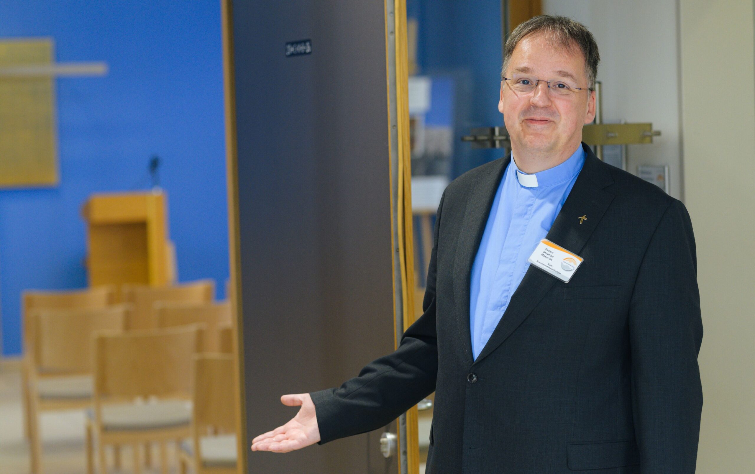 Porträtaufnahme von einem Priester vor einer Krankenhauskapelle