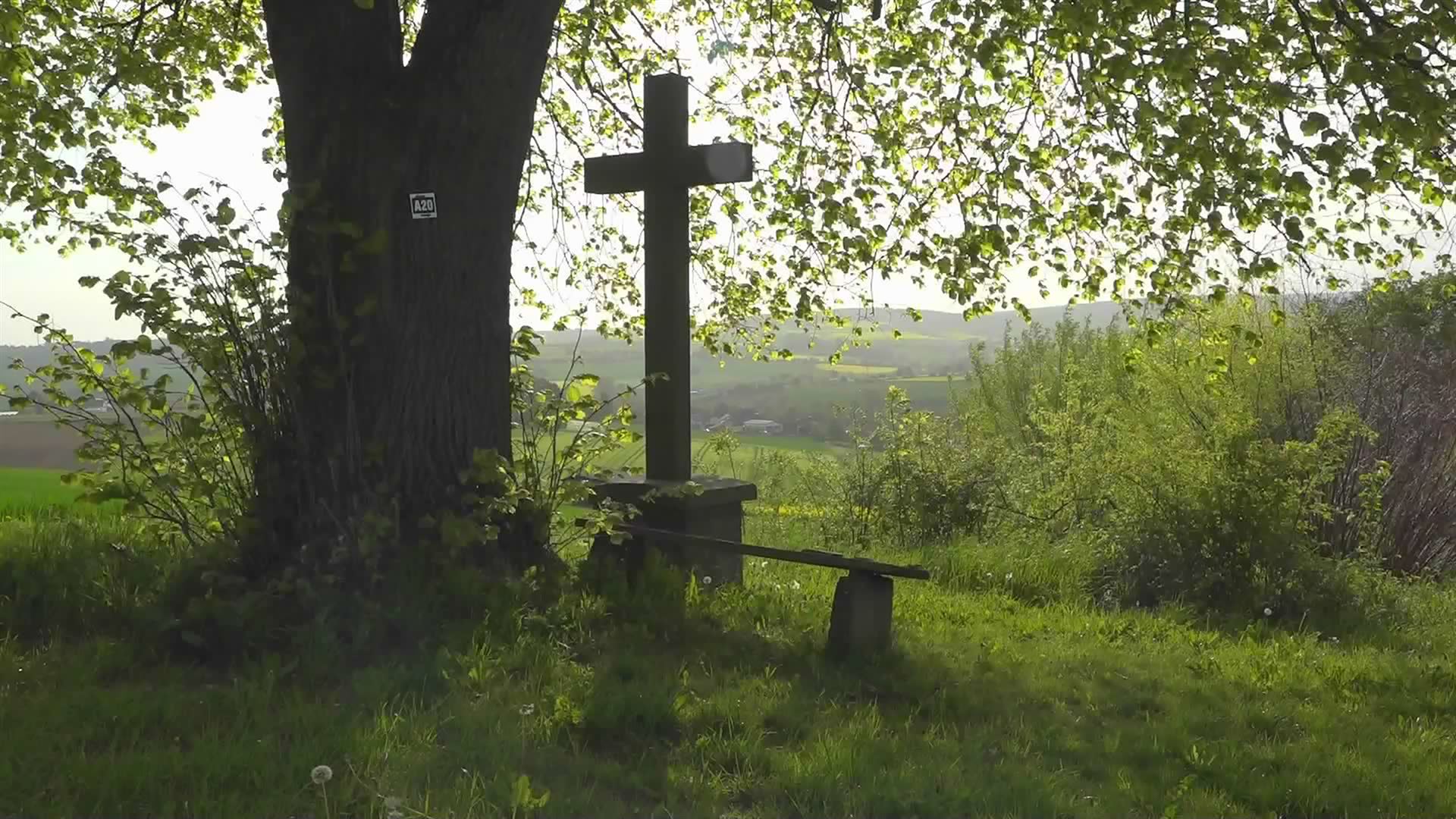 Ein Kreuz neben einer Bank lädt zum Innehalten mit Blick auf die Landschaft ein.
