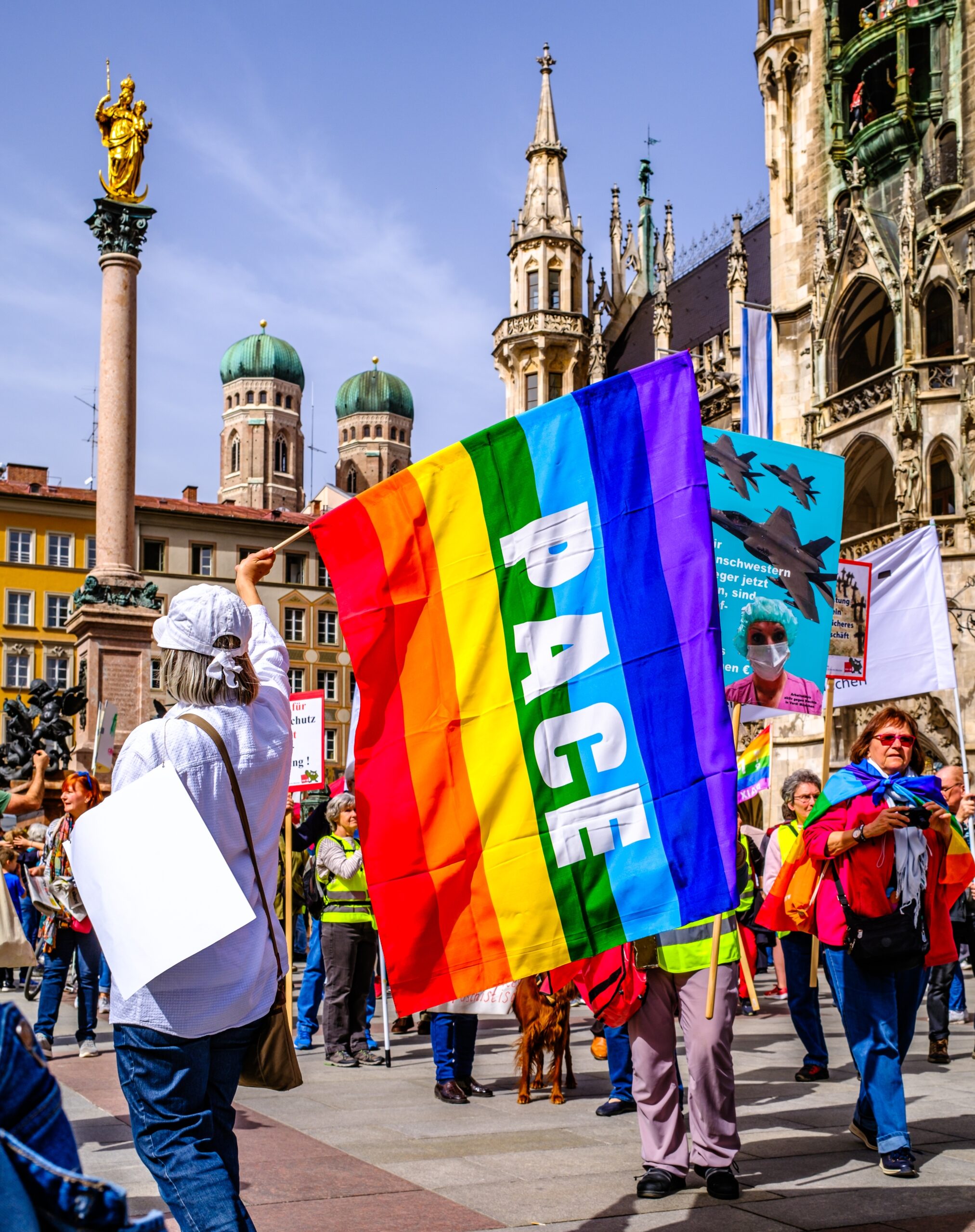 Menschen schwenken Pace-Fahnen beim Ostermarsch in München 2024.